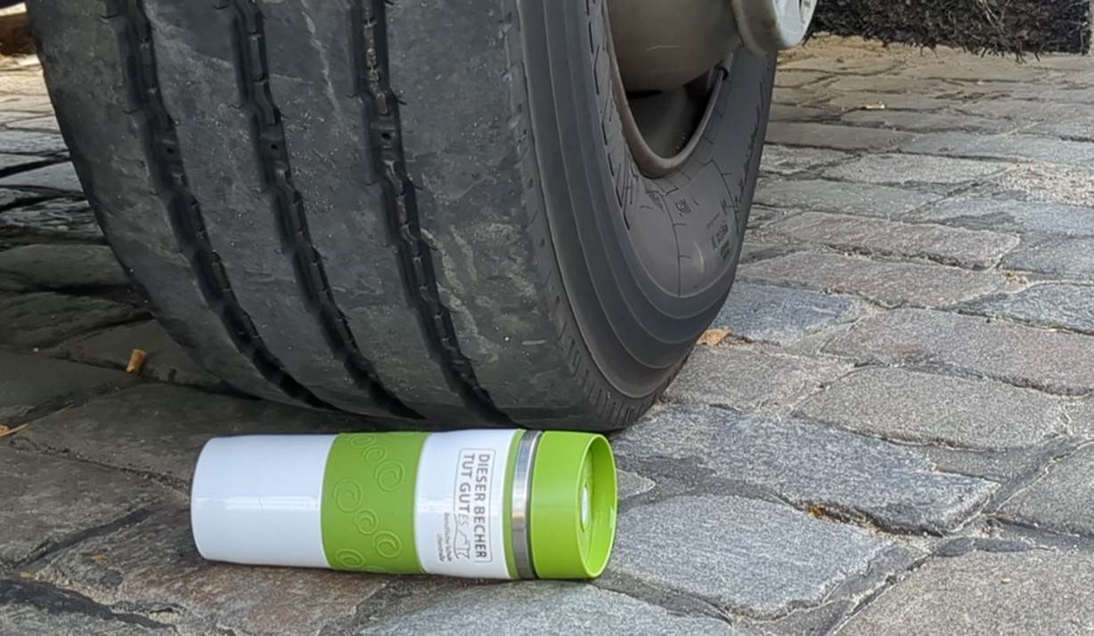 Nahaufname eines Mehrwegbechers neben einem Autoreifen