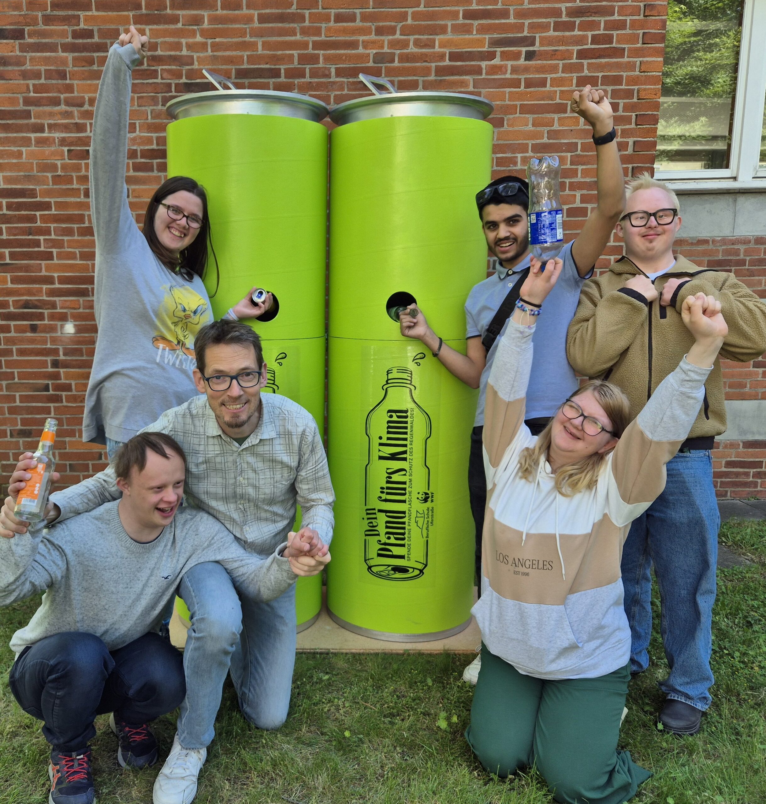 Jubelnde Schüler vor zwei XXL-Pfandsammel-Dosen